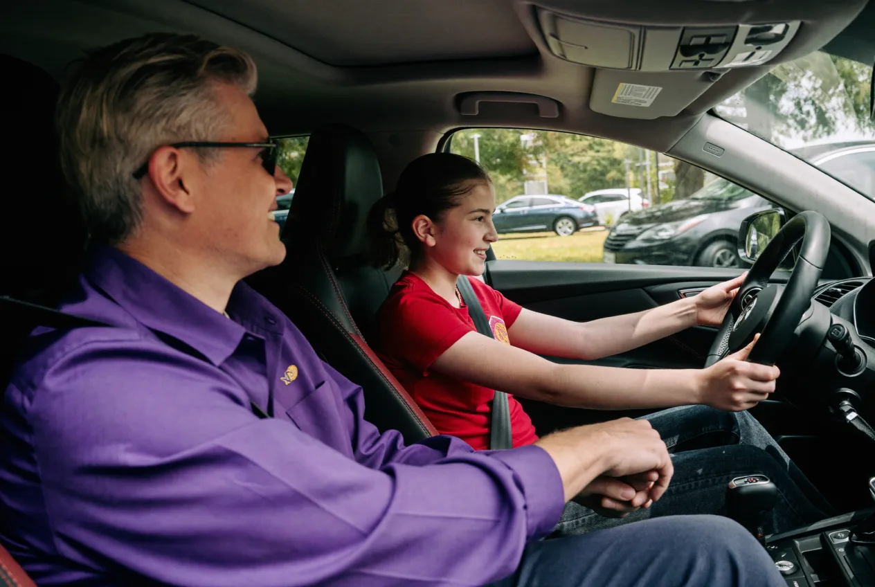 Fahrlehrer erklärt einem Fahrschüler entspannt die nächste Übung am Fahrzeug